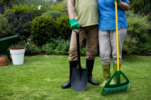 Sección baja de pareja senior de pie con herramientas de jardín