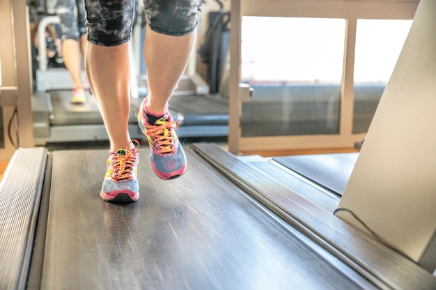 Foto sección baja de una persona corriendo en una cinta de correr en el gimnasio