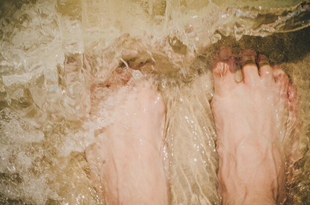 Foto sección baja de una persona de pie en el agua en la playa