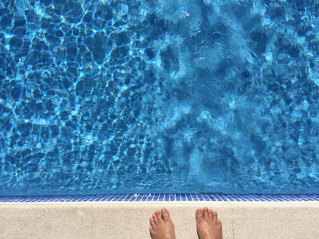 Sección baja de una persona de pie junto a la piscina
