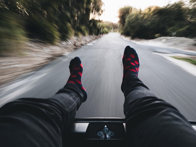 Sección baja de una persona relajándose en un coche en movimiento en la carretera