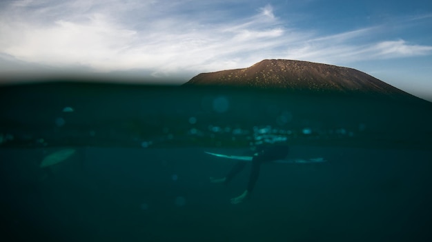 Sección baja de una persona con una tabla de surf en el mar contra el cielo