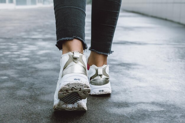 Sección baja de una persona con zapatos blancos caminando por la carretera