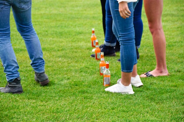 Foto sección baja de personas con botellas de pie en el campo