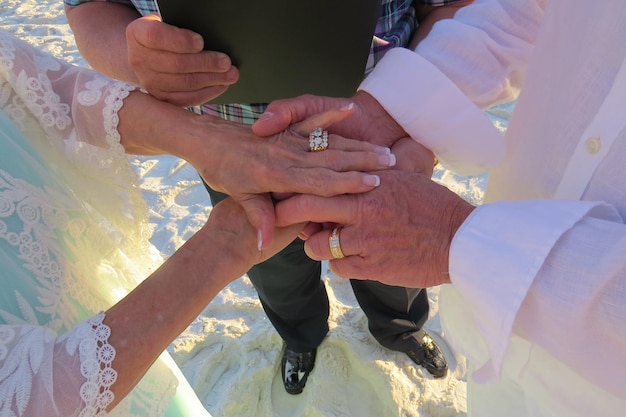 Sección baja del sacerdote con la novia y el novio tomados de la mano mientras están de pie en la playa durante la ceremonia de la boda