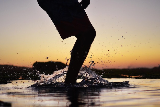 Sección baja de la silueta de un hombre de pie en el mar durante la puesta de sol