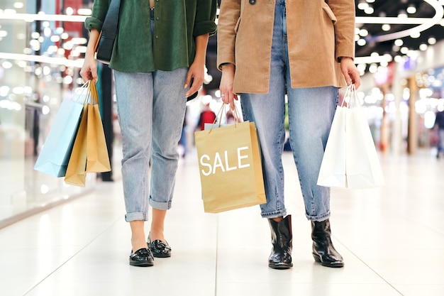 Bajo la sección de dos mujeres jóvenes en ropa casual con bolsas de papel llenas de compras mientras recorre el escaparate el viernes negro