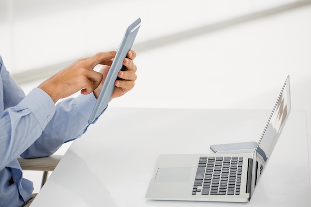 Sección intermedia del empresario con tableta digital con laptop en la mesa