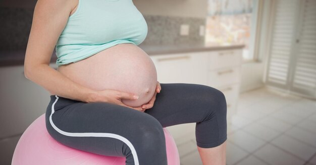 Sección intermedia de la mujer embarazada en la bola de ejercicio en la cocina borrosa