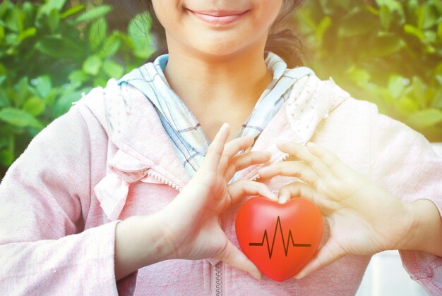 Foto sección media de una adolescente que sostiene una forma de corazón contra las plantas