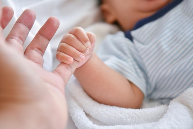 Sección media de un bebé sosteniendo la mano de la madre recortada en la cama