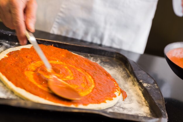 Sección media de un chef masculino preparando pizza