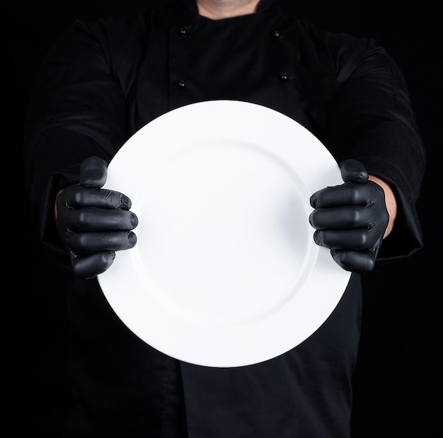 Foto sección media del chef sosteniendo un plato blanco vacío contra un fondo negro