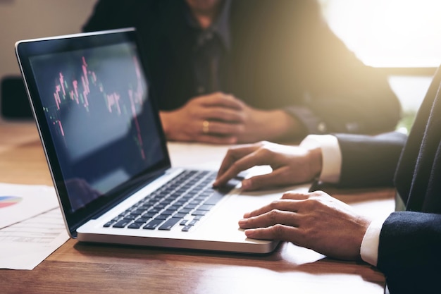 Sección media de colegas con computadora portátil y papeles de gráficos trabajando en el escritorio