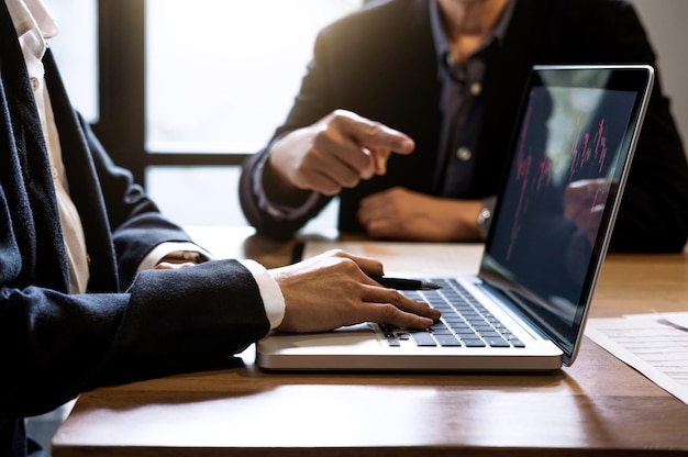 Sección media de colegas de negocios discutiendo mientras usan una computadora portátil en la mesa de la oficina