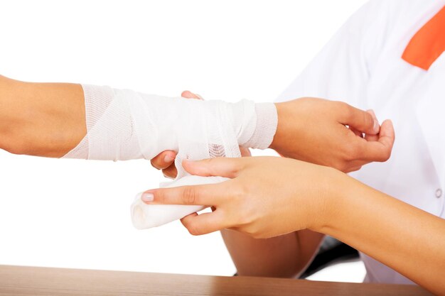 Sección media de una doctora aplicando un vendaje en la mano del paciente contra un fondo blanco