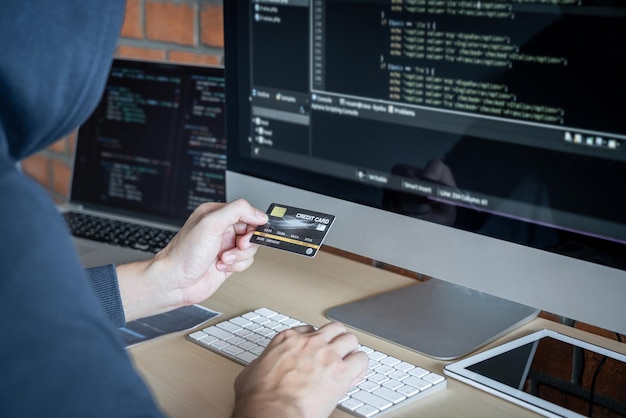 Sección media de un hacker sosteniendo una tarjeta de crédito mientras usa la computadora