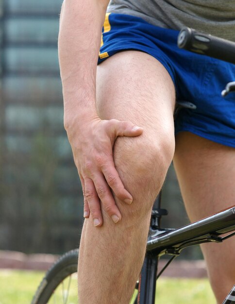 Foto sección media de un hombre con bicicleta tocando la rodilla en dolor