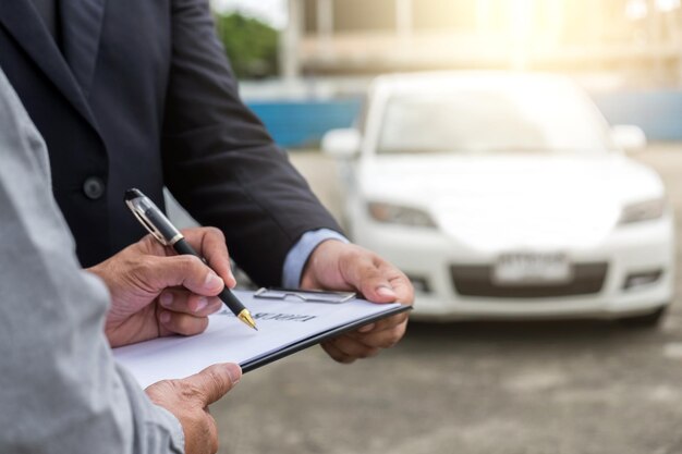 Foto sección media de un hombre firmando un papel con un hombre de negocios contra un coche