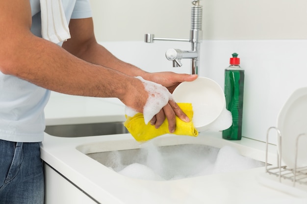 Sección media de hombre lavando los platos en el fregadero de la cocina