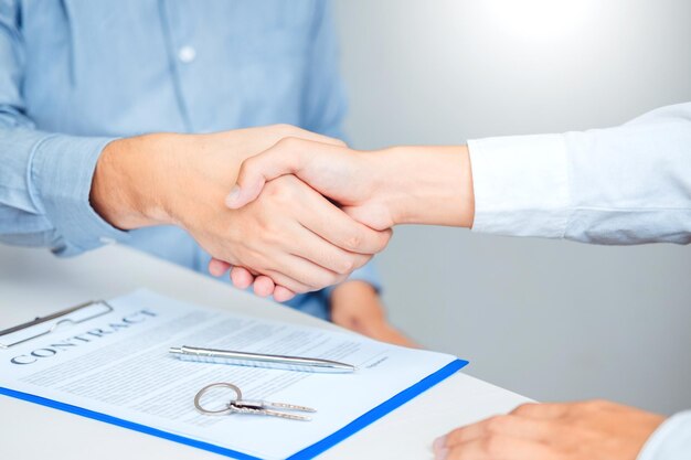 Foto sección media de un hombre y una mujer estrechando la mano por un papel de contrato con pluma y llave en la mesa