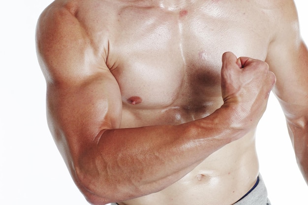 Foto sección media de un hombre musculoso sin camisa flexionando los músculos sobre un fondo blanco