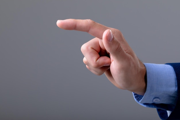 Sección media del hombre de negocios caucásico apuntando con el dedo, aislado sobre fondo gris. concepto de tecnología empresarial, comunicación y crecimiento.