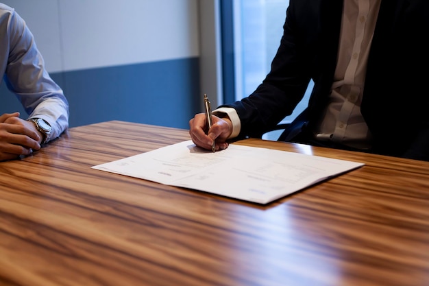 Sección media de un hombre de negocios con un colega escribiendo en un documento en una mesa en la oficina