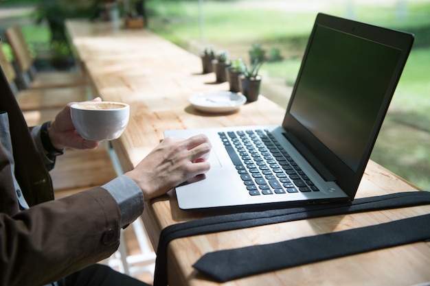 Sección media de un hombre de negocios sosteniendo una taza de café mientras trabaja en una computadora portátil