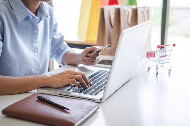 Sección media de un hombre de negocios usando una computadora portátil mientras sostiene una tarjeta de crédito trabajando en la mesa