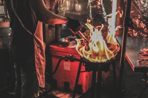 Sección media de un hombre preparando comida en un puesto de mercado durante la noche