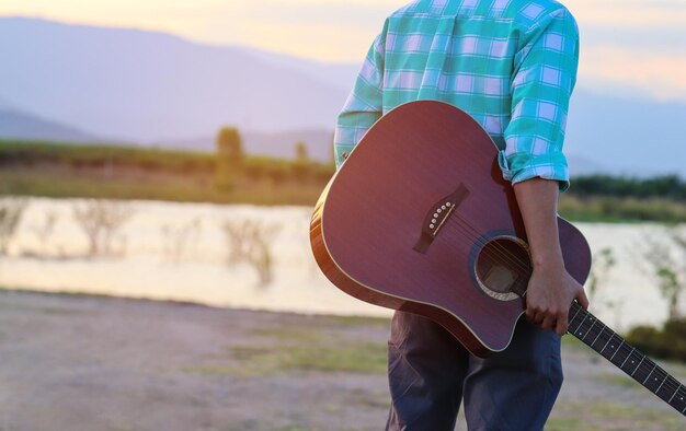 Sección media de un hombre que lleva una guitarra en la orilla del lago