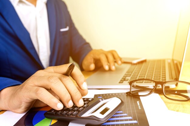 Foto sección media de un hombre que usa una calculadora mientras escribe en una computadora portátil en la mesa de la oficina