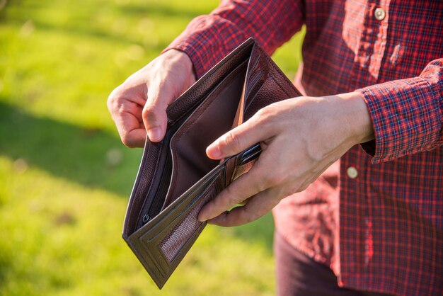 Sección media de un hombre sosteniendo una billetera vacía mientras está de pie en la hierba
