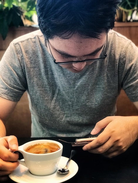 Foto sección media de un hombre sosteniendo café y usando un teléfono móvil