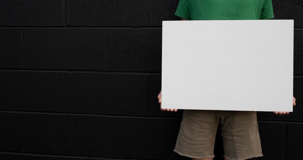 Sección media de un hombre sosteniendo un cartel en blanco mientras está de pie contra la pared