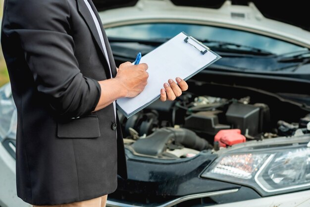 Foto sección media de un hombre sosteniendo un clipboard mientras está de pie contra un coche