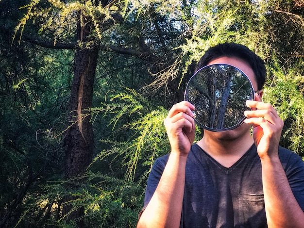 Foto sección media de un hombre sosteniendo un espejo en el bosque