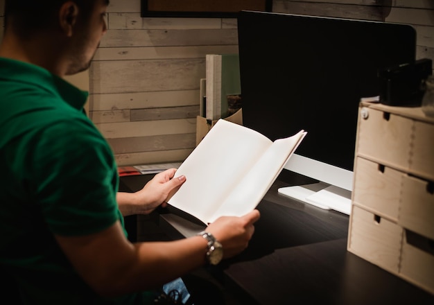 Sección media de un hombre sosteniendo un libro en blanco mientras está sentado en la mesa