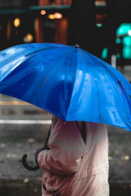 Foto sección media de un hombre sosteniendo un paraguas azul bajo la lluvia