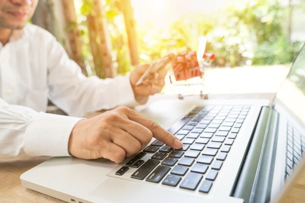 Sección media de un hombre sosteniendo una tarjeta de crédito mientras usa una computadora portátil en la mesa