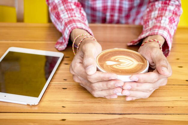 Sección media de un hombre sosteniendo una taza de café en la mesa