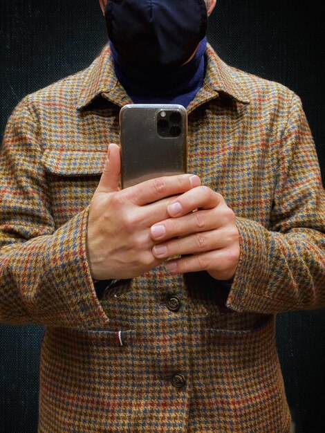 Foto sección media de un hombre sosteniendo un teléfono móvil mientras está de pie contra un fondo negro