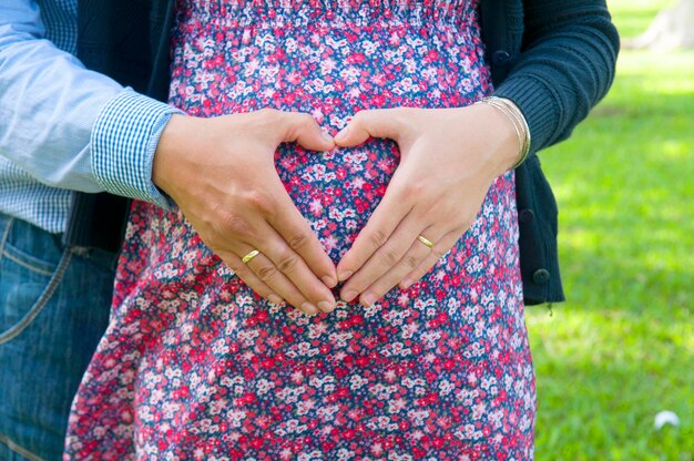 Foto sección media de un hombre con su esposa embarazada haciendo forma de corazón en el vientre