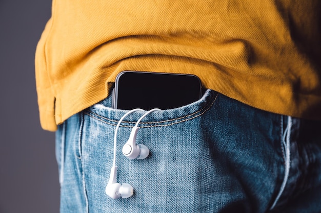 Sección media de un hombre con teléfono móvil y auriculares en el oído en el bolsillo