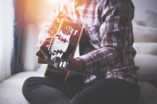 Foto sección media de un hombre tocando la guitarra mientras está sentado en el asiento en casa