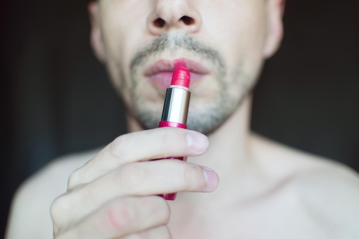 Foto sección media de un hombre transgénero aplicando lápiz labial rojo