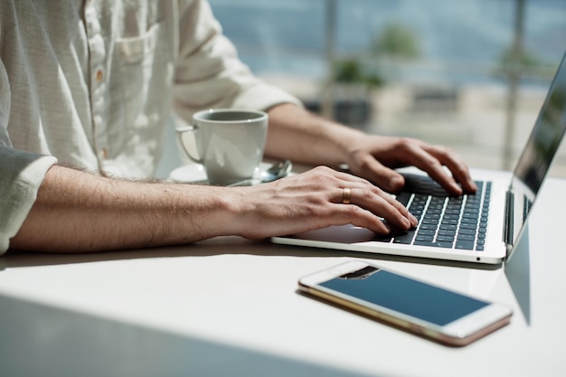 Sección media de un hombre usando una computadora portátil mientras toma café en una mesa en una cafetería