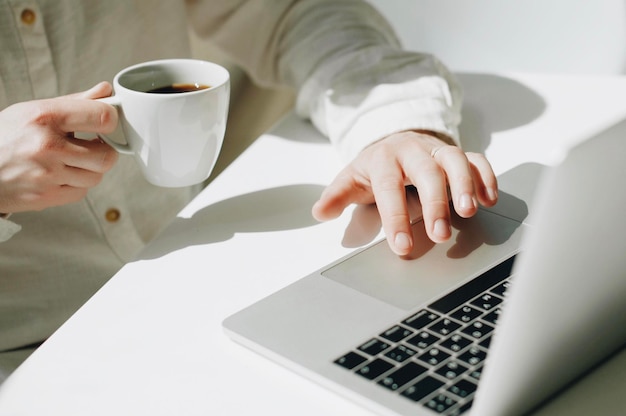 Sección media de un hombre usando una computadora portátil mientras toma café en una mesa en una cafetería