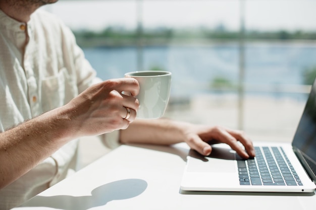 Sección media de un hombre usando una computadora portátil mientras toma café en una mesa en una cafetería